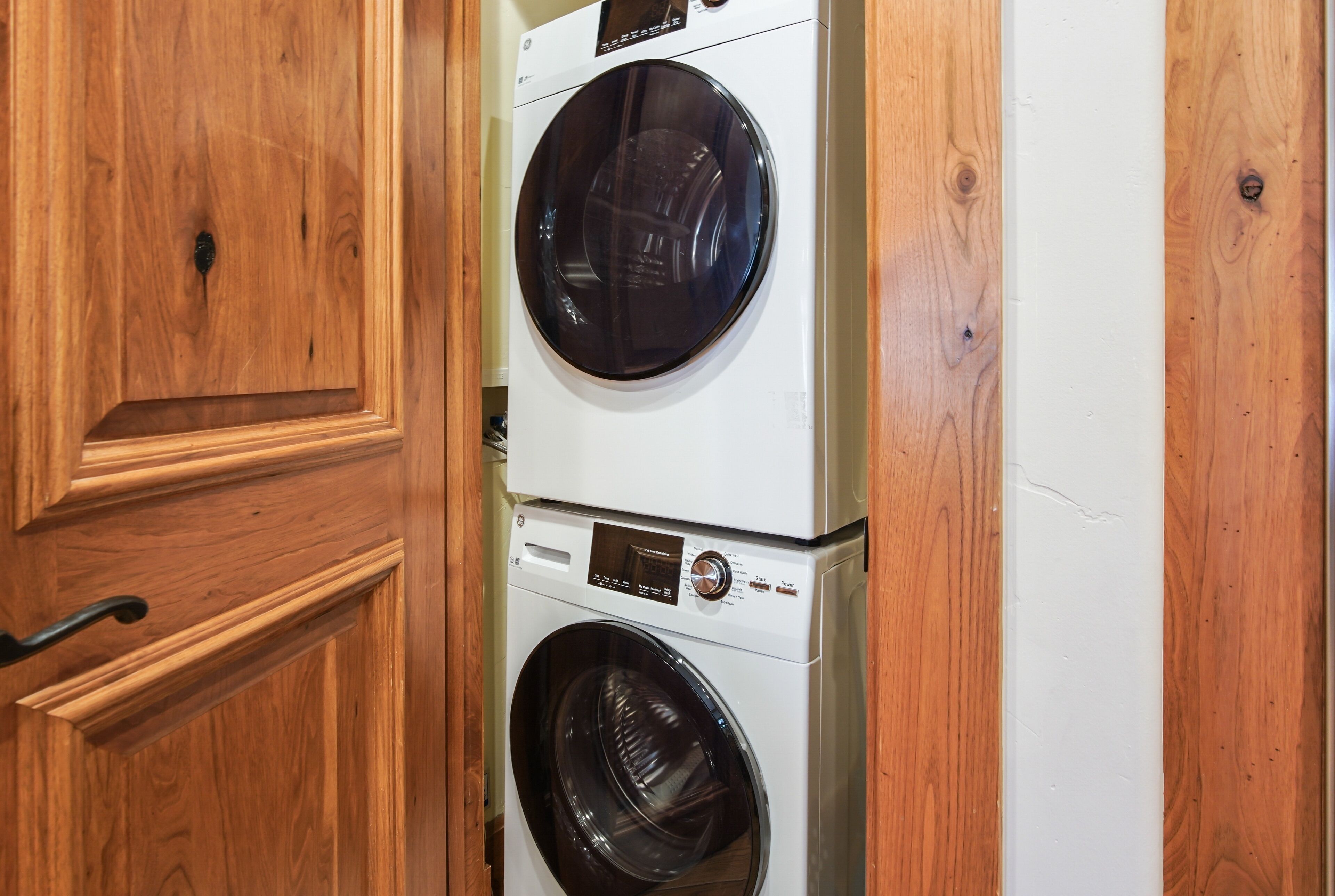 Un appareil combiné lave-linge et sèche-linge, de type « superposé », intégré dans un meuble en bois.