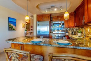 A kitchen with a granite countertop, wooden cabinets, and a built-in oven. - Kihei Akahi D-510 1 Bedroom Condo (Kihei)
