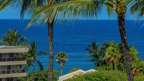 A multi-story building with balconies overlooking a coastal area with palm trees and the ocean.