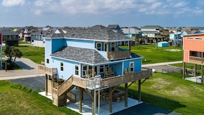 A two-story house with a balcony and a deck, surrounded by a grassy area and other houses.