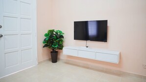 A room with a white door, a potted plant, a mounted TV, and a white console unit against a peach-colored wall. - Peach Homestay Bandar Tasik Puteri (Rawang)