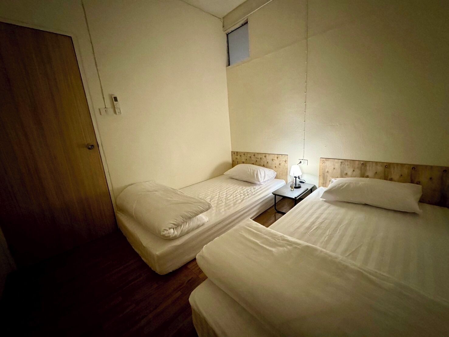 A hotel room with two single beds, a wooden door, and a small window.