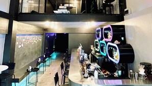 Un área de bar moderna con una barra larga, varios taburetes y una zona de cocina a la vista, con una máquina de café.