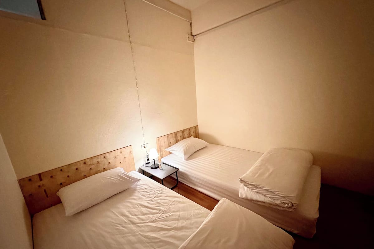 Habitación de hotel con dos camas, una mesita de noche y una lámpara colgante.