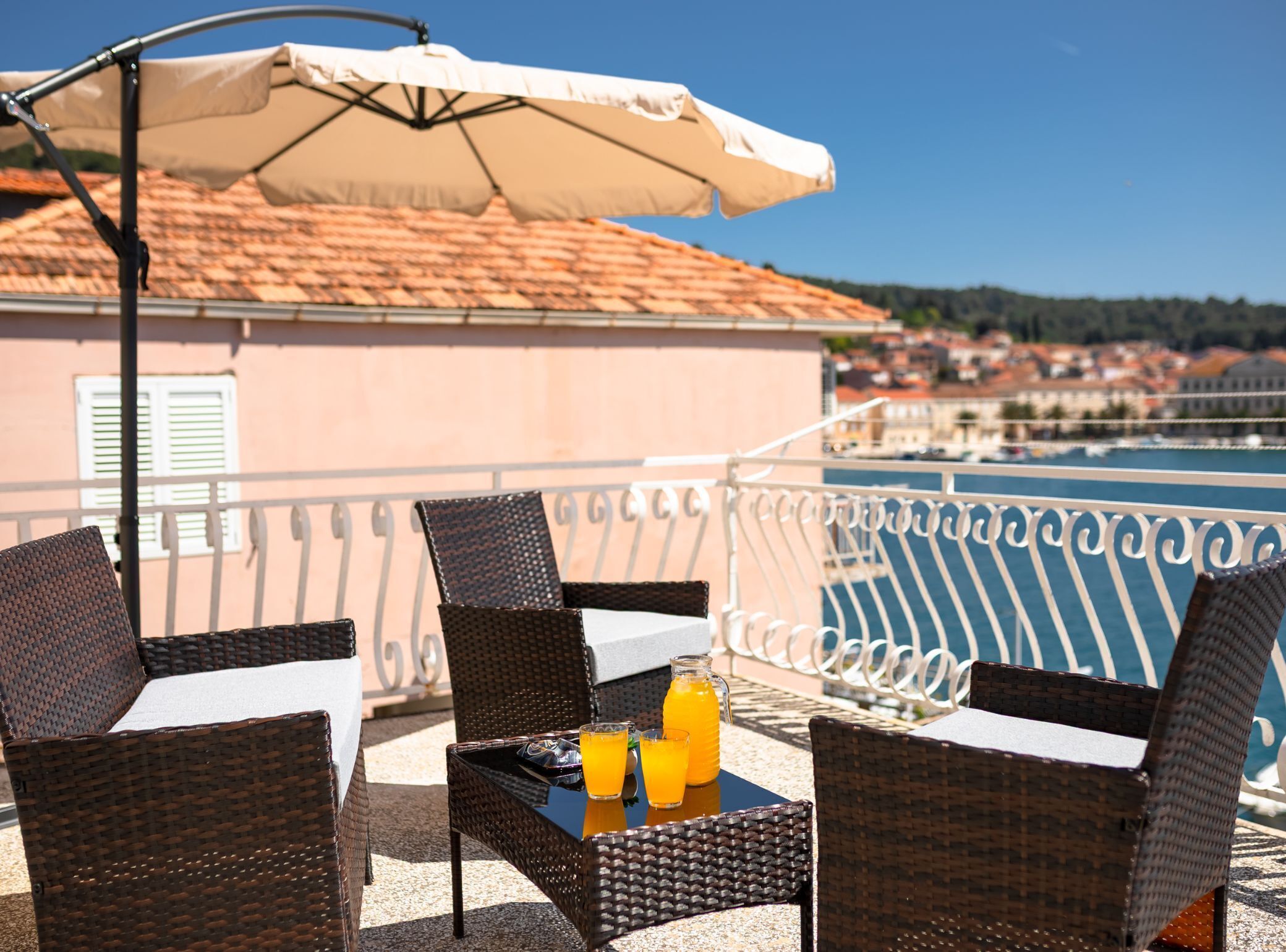 A terrace with wicker furniture, a table with a drink, and a view of a town and sea.