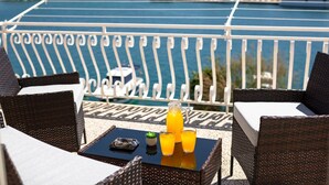 A balcony with wicker furniture, a table with a drink, and a view of the sea and buildings in the background. - Seaside Apartment Franica (Vela Luka)