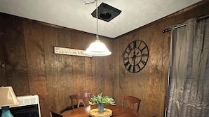 A dining area with a wooden table, chairs, a hanging light fixture, a clock, and a sign that reads "Welcome to the".