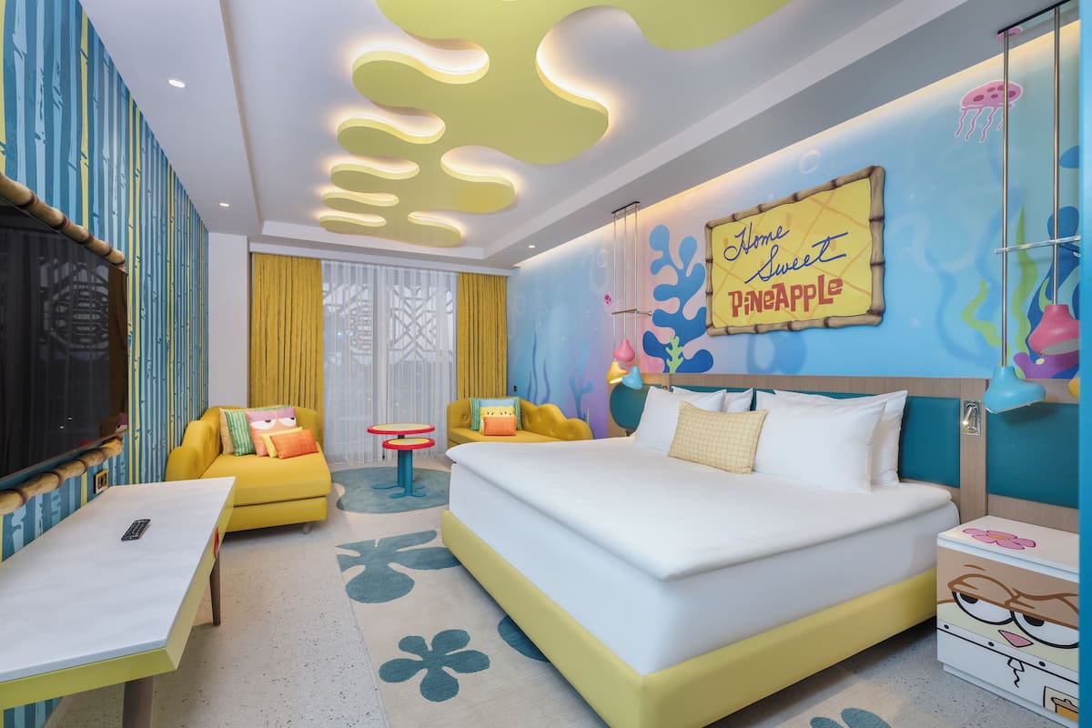 Una habitación de hotel con una cama, un sofá amarillo, una mesita y un cartel decorativo en la pared.