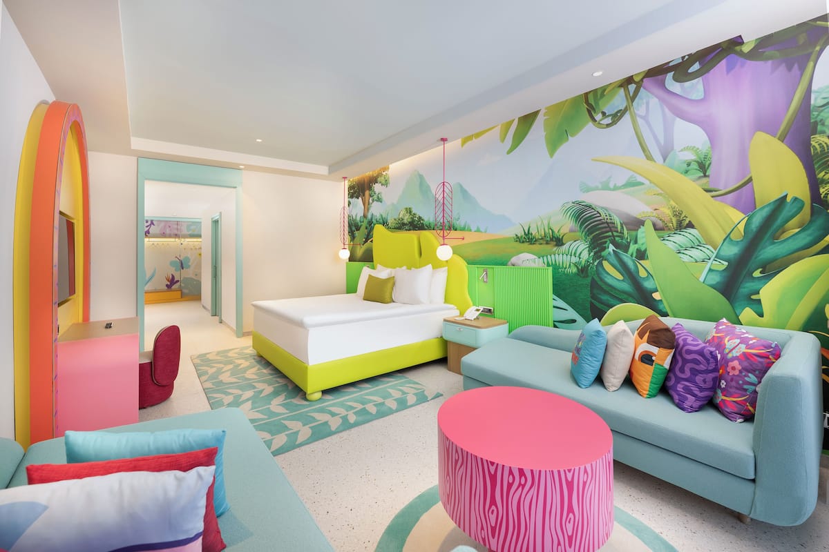 Una habitación de hotel vibrante con una cama, un sofá, una mesa de centro y un mural con una escena de selva.