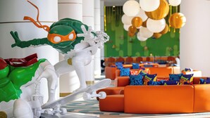 A modern lobby with a green wall, orange seating, and a white robot figure. - The Land of Legends Nickelodeon Hotels Antalya (Serik)