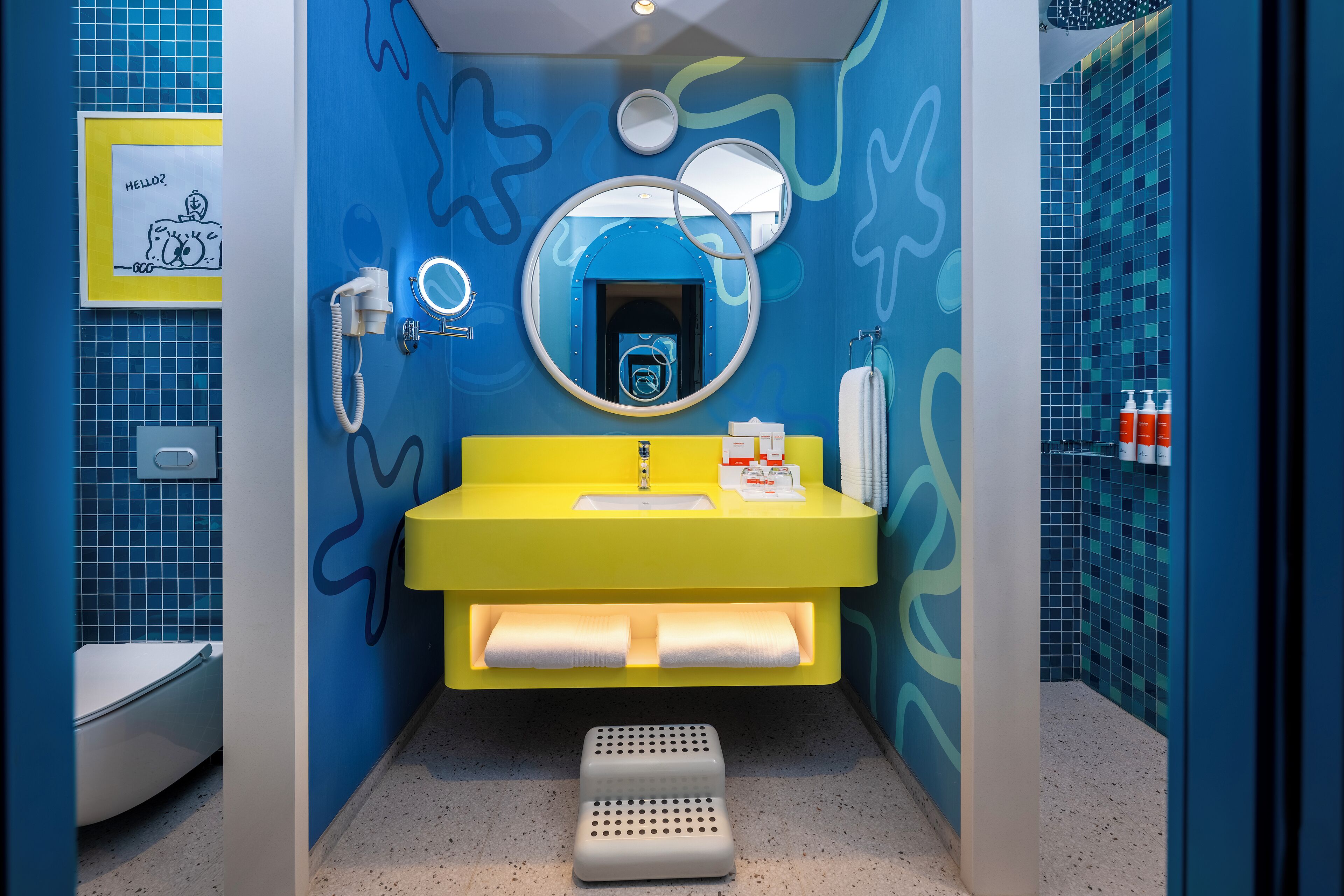 Un baño con un lavamanos amarillo, un espejo, un inodoro y una zona de ducha.