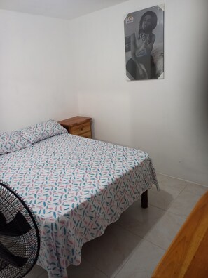 Ein Schlafzimmer mit einem Bett, einem Nachttisch, einem Bild an der Wand und einem Sessel.