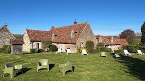 A stone building with a red-tiled roof, surrounded by a grassy lawn with several white lounge chairs. - Gite with heated indoor pool on the Opal Coast (Tingry)