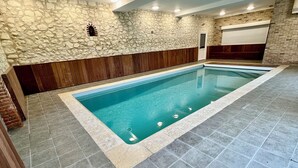 A swimming pool with stone walls and wooden paneling, surrounded by tiled flooring. - Gite with heated indoor pool on the Opal Coast (Tingry)