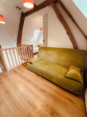 A loft-style room with a wooden floor, a green sofa, a wooden railing, and a sloped ceiling with exposed beams.