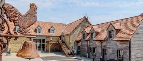 A courtyard with a stone building featuring a red-tiled roof, a wooden staircase, and a bell.