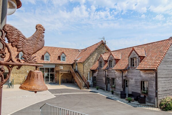 A courtyard with a stone building featuring a red-tiled roof, a wooden staircase, and a bell. - Vacation home with a heated indoor pool on the Opal Coast (Tingry)