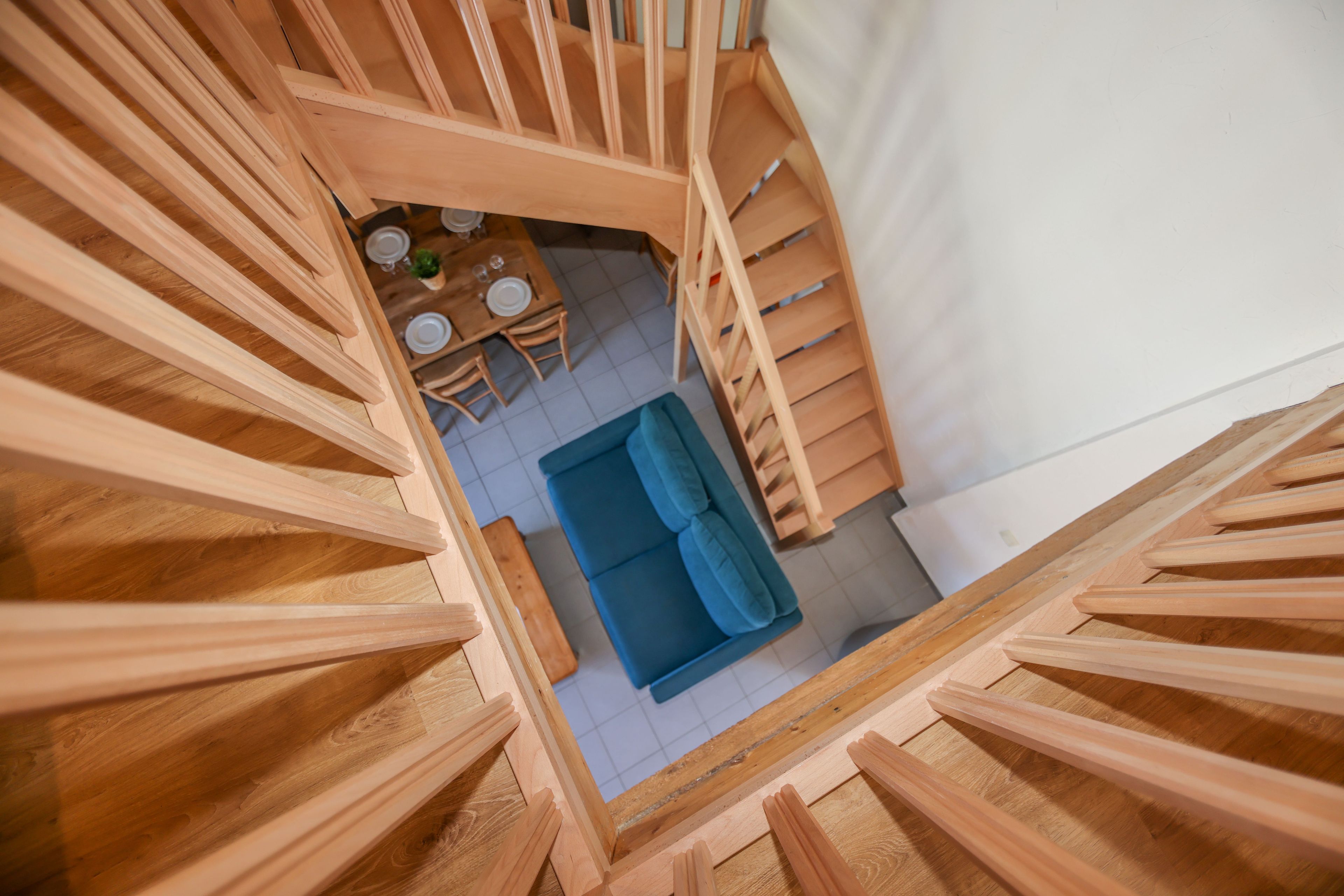 Una escalera de madera lleva a un comedor con un sofá azul y una mesa preparada para cuatro comensales.