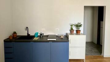 Una cucina compatta con un piano di lavoro nero, un lavandino e un piccolo armadietto. Sul piano di lavoro ci sono piante in vaso e, a destra, un armadietto bianco.