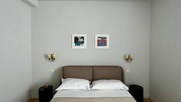 Camera da letto minimalista con un letto, due lampade a parete e due quadri appesi.