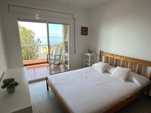 Une chambre à coucher avec un lit, une petite table de chevet, une chaise près de la fenêtre et une vue sur l’extérieur.