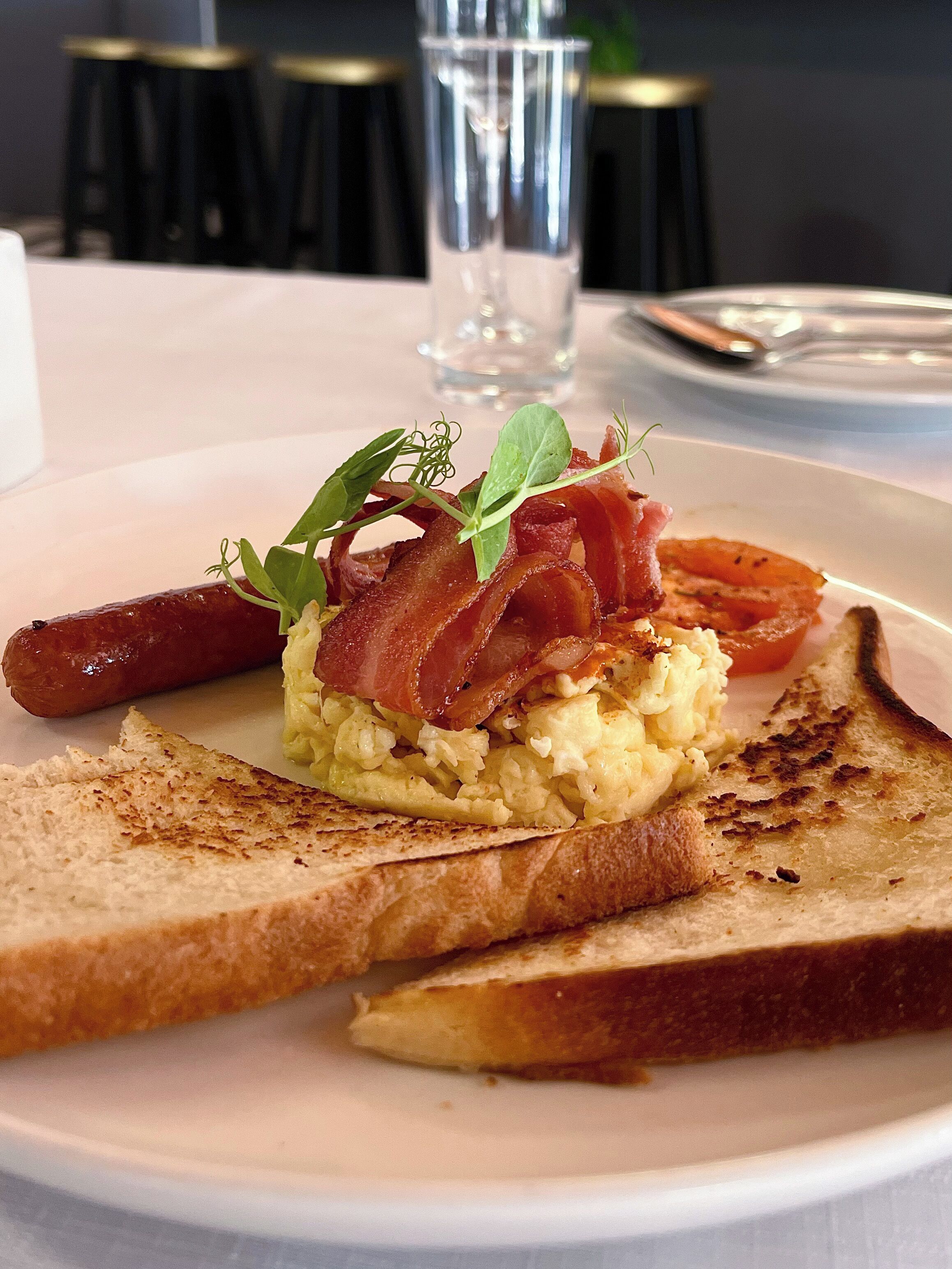 A breakfast plate with scrambled eggs, bacon, sausage, and toast.