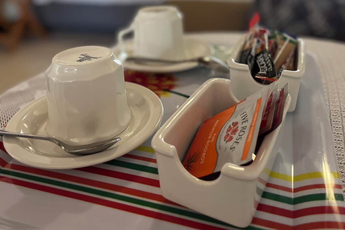 A breakfast tray with a cup, saucer, spoon, and a container of pastries on a striped tablecloth in a hotel room.
