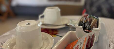 Un plateau de petit-déjeuner avec une tasse, une soucoupe, une cuillère et une boîte de viennoiseries, posé sur une nappe à rayures dans une chambre d'hôtel.