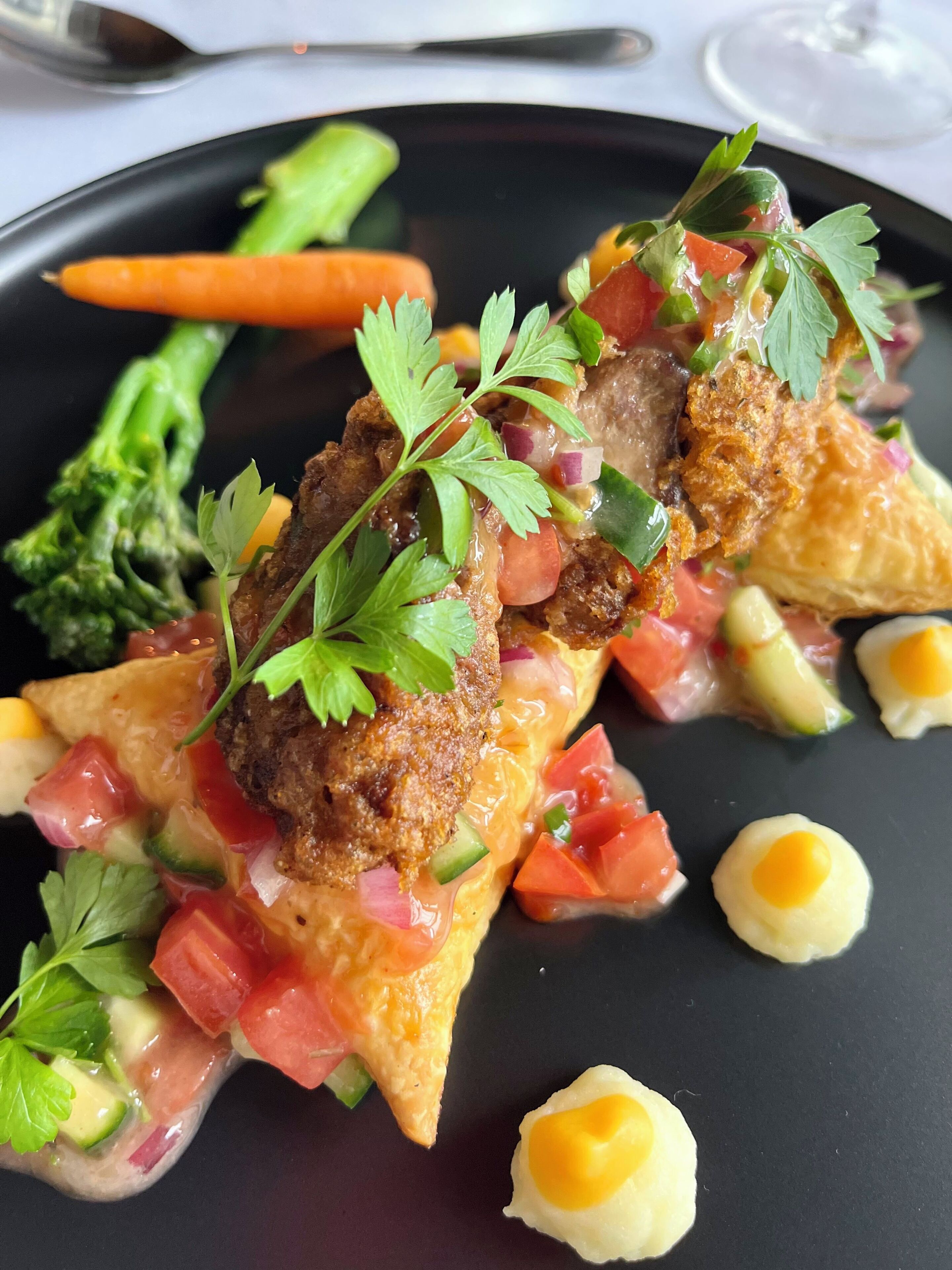 Un plat composé de viande, de légumes et de quelques accompagnements, le tout présenté dans une assiette noire.