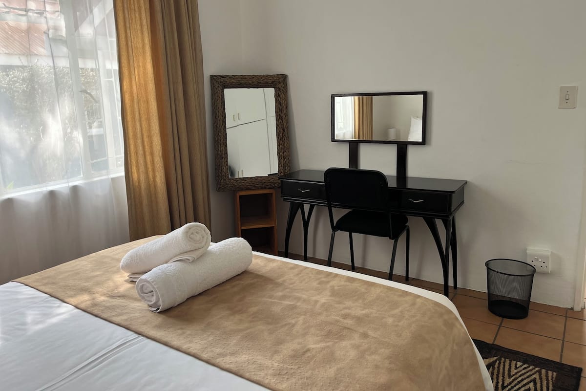 A hotel room with a bed, a desk, a chair, a mirror, and a window with curtains.