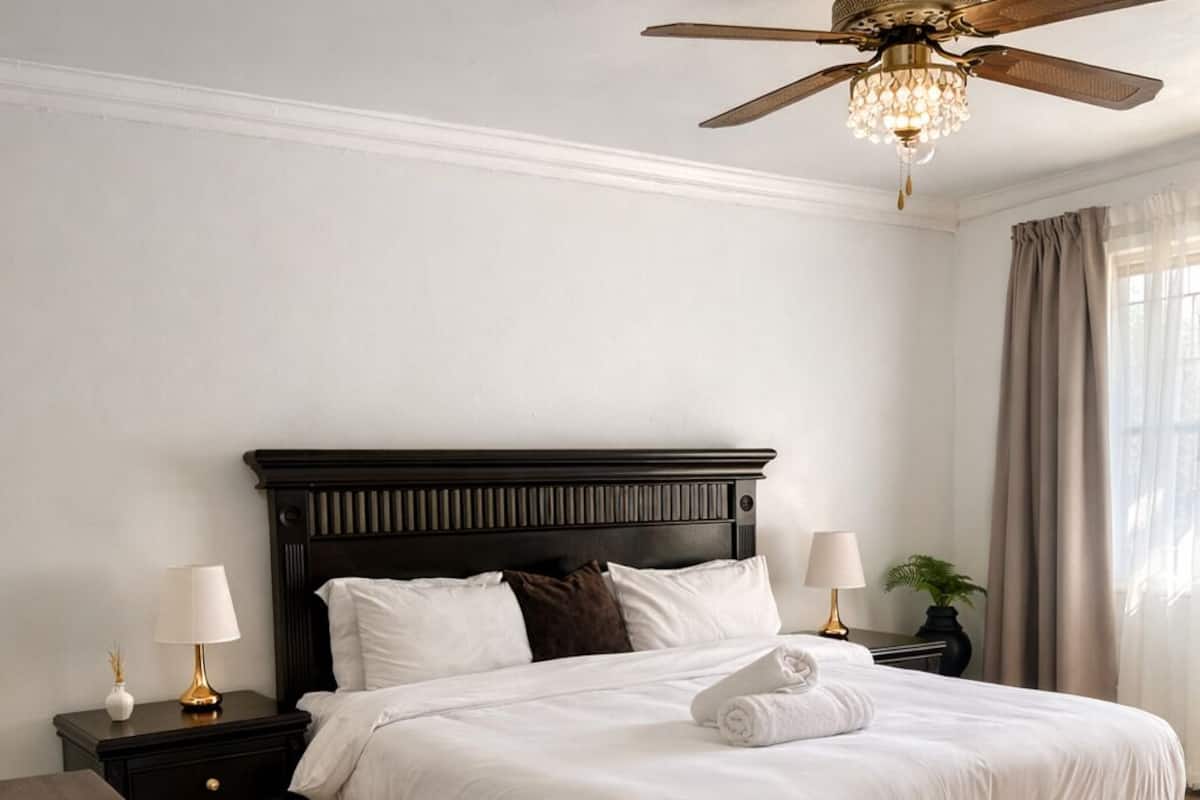 A bedroom with a dark wood bed, white bedding, a ceiling fan, and a nightstand with a lamp.