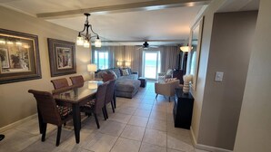 A spacious living room with a large sofa, a dining area with a glass-top table, and a ceiling fan.