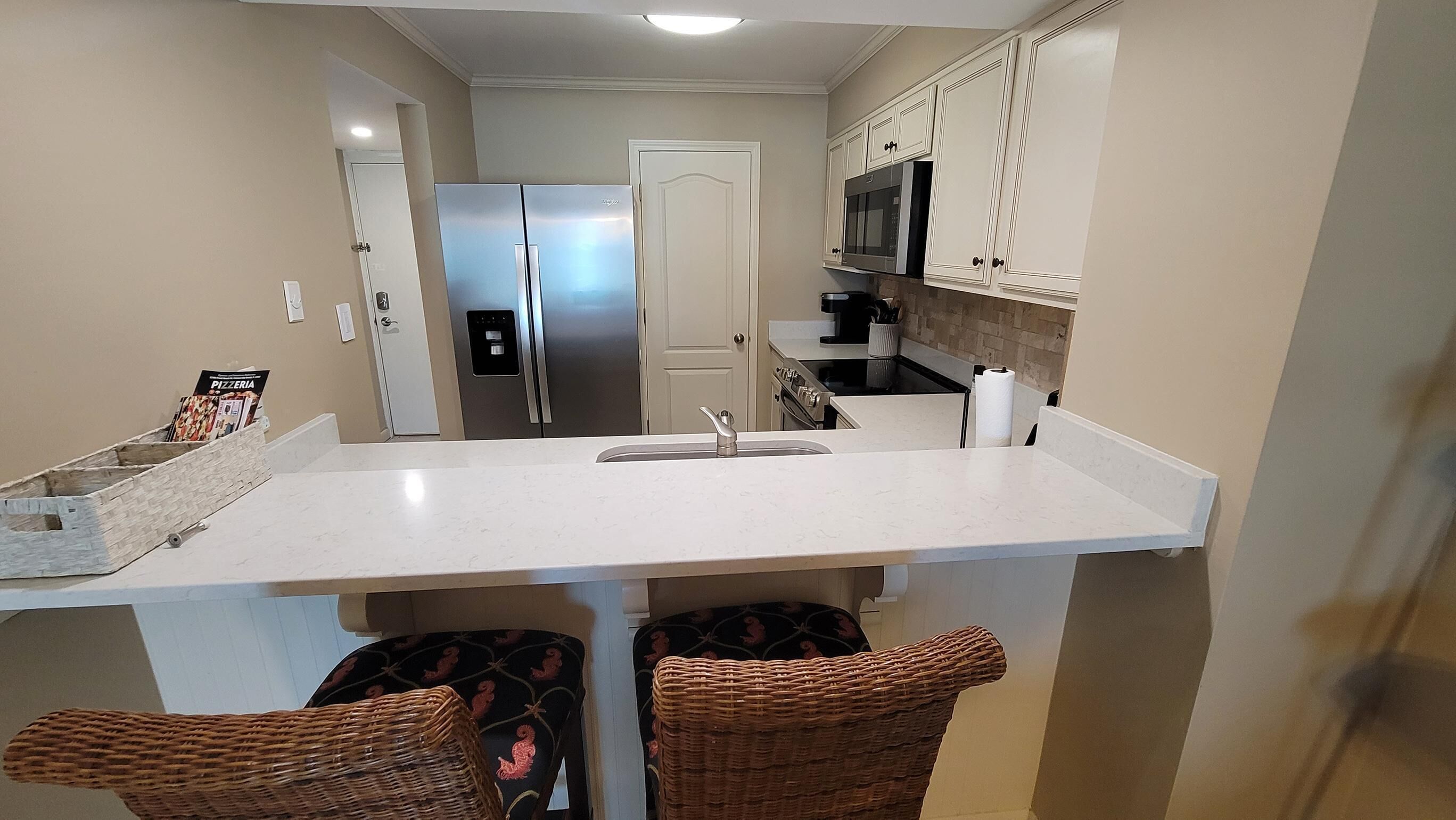 A kitchen with a central island, stainless steel appliances, and wicker chairs.