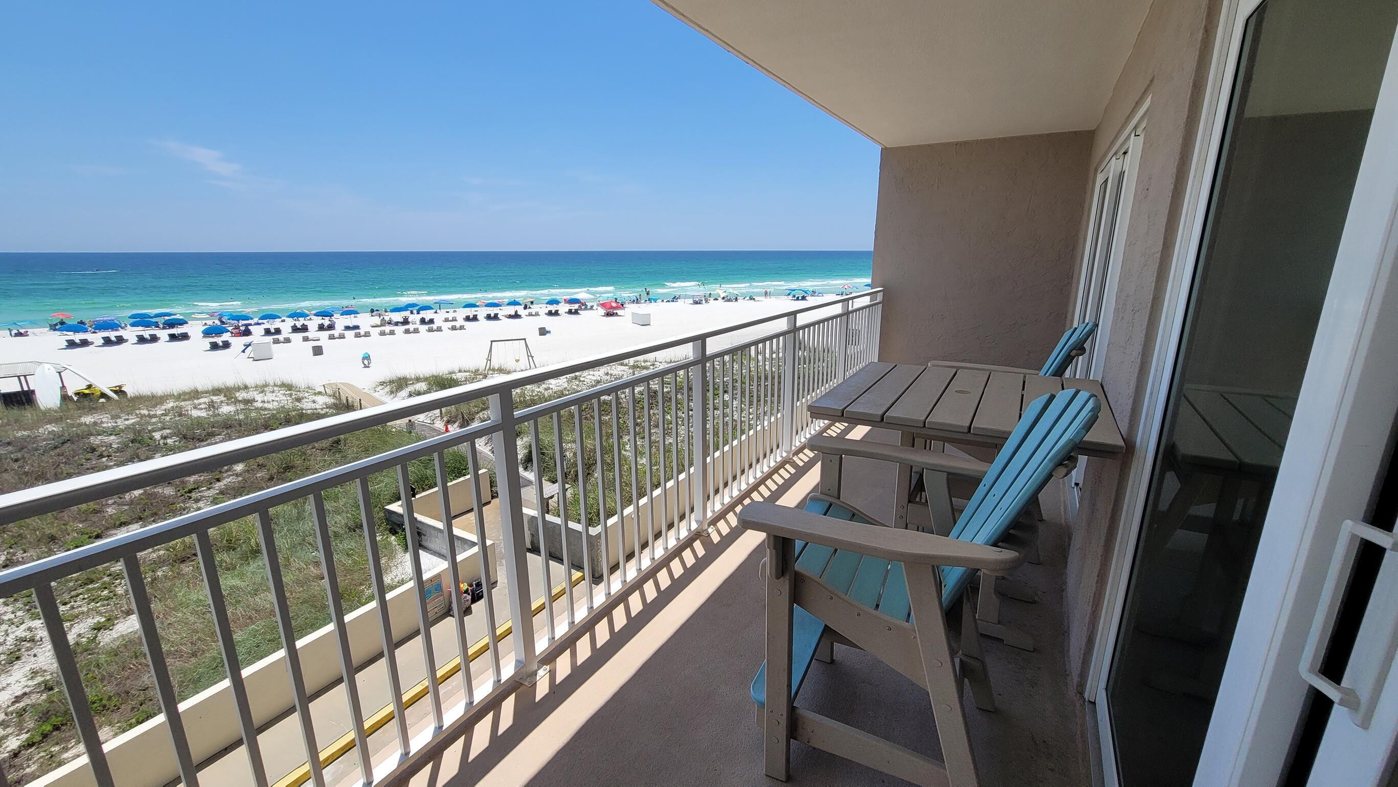 A balcony with a view of a beach, a table, and two chairs.
