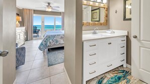 A bedroom with a balcony, a bathroom with a vanity, and a view of the ocean.