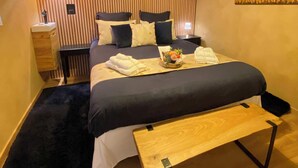 Une chambre à coucher moderne avec un grand lit, des tables de chevet, un banc et un luminaire fixé au mur.