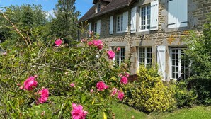 Une maison en pierre avec de nombreuses fenêtres et un jardin où poussent des fleurs roses.