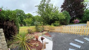 Un sentier de jardin bordé d’une clôture en bois, agrémenté de diverses plantes et d’un mur en pierre.