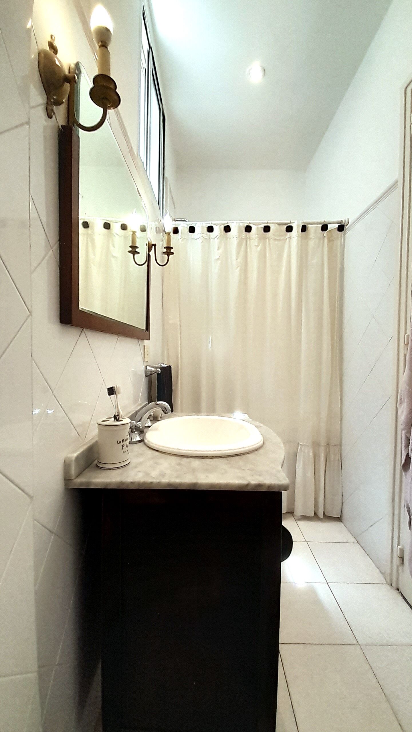 Un baño con lavamanos blanco, espejo, toallero y cortina de ducha.