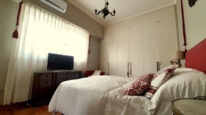 A bedroom with a bed, a TV on a stand, a wardrobe, and a chandelier.