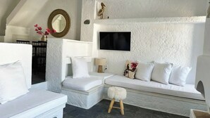 A modern living room with a white sofa, a small stool, and a television mounted on the wall.