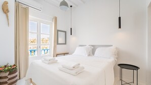 A hotel room with a large bed, a small side table, a hanging pendant light, and a view of the outside.
