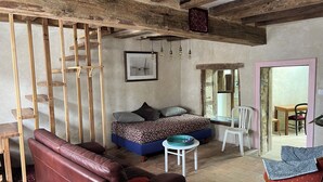A cozy room with a wooden ceiling, a bed with patterned bedding, a leather sofa, a small table, and a chair. - 1 Bedroom Private vacation home in SoulignÃ©-sous-Ballon (Souligné-sous-Ballon)