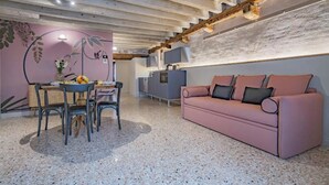 Un salon chaleureux avec un canapé rose, une table à manger avec des chaises et un coin cuisine équipé d’un réfrigérateur et de placards.