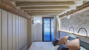 Une chambre à coucher avec un lit, des poutres en bois, une fenêtre donnant sur un beau paysage et un luminaire fixé au mur.