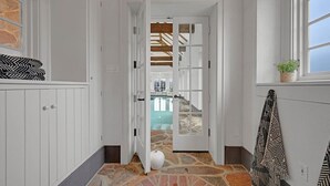 A narrow hallway with white walls and a stone floor leading to a room with a wooden ceiling and a window. - Roundtop Mansion Breathtaking View indoor Pool (Wrightsville)