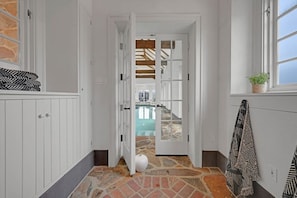 A narrow hallway with white walls and a stone floor leading to a room with a wooden ceiling and a window. - Roundtop Mansion Breathtaking View indoor Pool (Wrightsville)