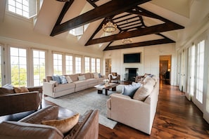 A spacious living room with a large sectional sofa, a fireplace, and a high ceiling with exposed beams.