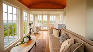 A spacious room with large windows, a wooden ceiling, a sofa, a telescope, and a view of greenery. - Roundtop Mansion Breathtaking View indoor Pool (Wrightsville)