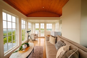 A spacious room with large windows, a wooden ceiling, a sofa, a telescope, and a view of greenery. - Roundtop Mansion Breathtaking View indoor Pool (Wrightsville)